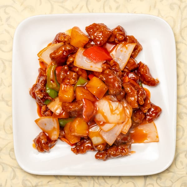 Sweet and sour chicken with pineapple, onions, and bell peppers on a white plate.