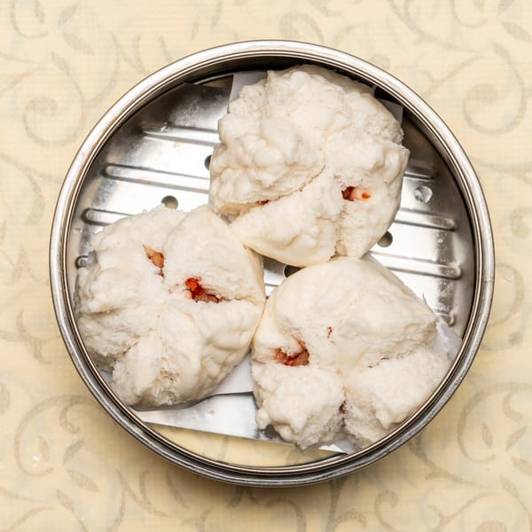 Three fluffy white char siu bao (steamed pork buns) in a metal dim sum steamer basket.